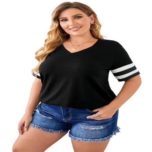 Woman wearing a black t-shirt with white sleeves and denim shorts indoors.